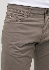 Beige katoenbroek met een slim fit, voorzakken en een klein merklogo op de zak. De stof heeft een gladde textuur.