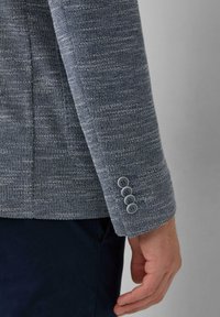 Grauer, strukturierter Blazerärmel mit vier Knopfakzenten, der ein gewebtes Stoffdesign und eine maßgeschneiderte Passform aufweist.