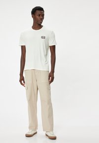 Hvid kortærmet t-shirt med teksten "NEW YORK", parret med lysebeige cargo-bukser med lommer. Modellens iført hvide sneakers.