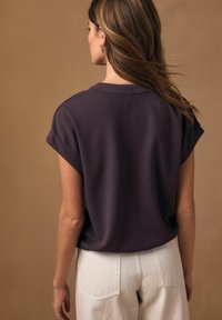 Tričko s krátkými rukávy v tmavě fialové barvě s volným střihem, kulatým výstřihem a ohrnutými rukávy, doplněné světlými kalhotami s vysokým pasem.