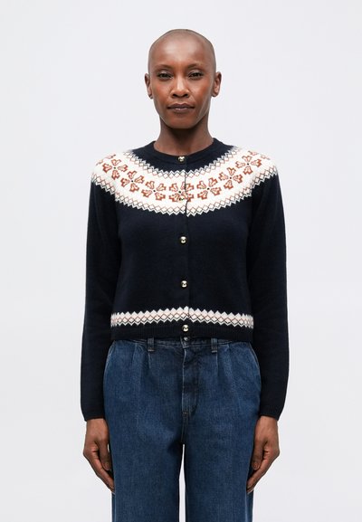 Gilet marine avec un empiècement à motif présentant des designs floraux blancs et rouille. Il a un col arrondi et des boutons dorés sur le devant.