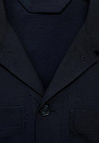 Marineblazer aus strukturiertem Stoff, mit Revers, einem einzigen Knopfverschluss und seitlichen Taschen. Das Gesamtdesign ist maßgeschneidert und klassisch.