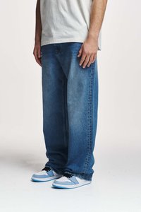 Blå denim baggy jeans med en falmet vask, kombinert med hvite og lyseblå joggesko, iført en løs hvit T-skjorte.