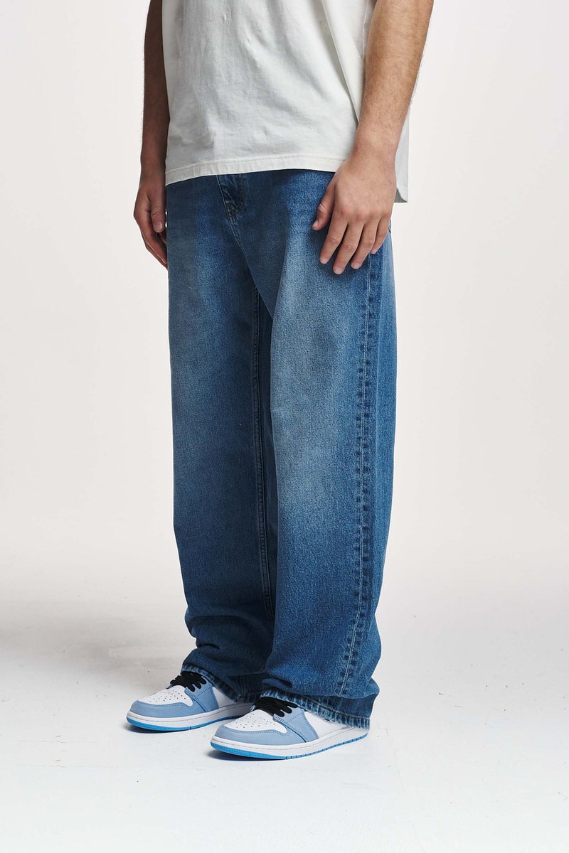 Blå denim baggy jeans med en falmet vask, kombinert med hvite og lyseblå joggesko, iført en løs hvit T-skjorte.