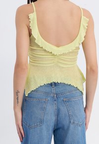 Top amarillo claro con volantes y escote en la espalda, acompañado de unos jeans de mezclilla azul con bolsillos traseros.