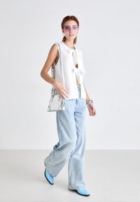 Hvit ermeløs topp med bånddetalj, blå jeans, blå spisse sko, sølvveske med dekorative aksenter, og lilla solbriller.