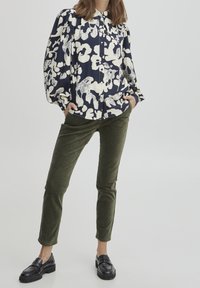 Blusa blu navy con motivo floreale e maniche a sbuffo, chiusura frontale a bottoni; abbinata a pantaloni in corduroy verde oliva e mocassini neri.