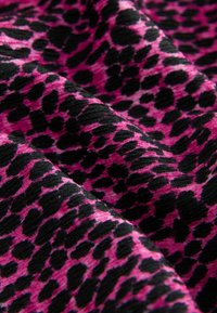 Rosa och svart leopardmönstrad tyg med ribbad textur, med varierande fläckstorlekar och en mjuk, slät yta.