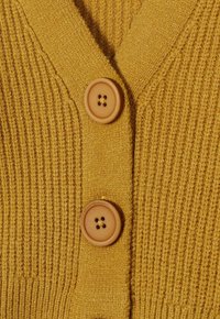 Cardigan jaune présentant une texture côtelée, un décolleté en V et trois boutons beiges à quatre trous chacun pour la fermeture.