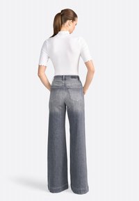 Hvid ribbet bodysuit med bølgende kant, parret med højlivet, bredbenede grå jeans med slid og baglommer.