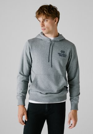 Sudadera gris hecha de tejido suave, con un bolsillo canguro frontal, capucha con cordón y un logo negro de "Red Bull Racing" en el pecho.