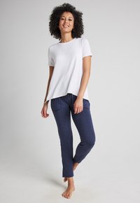Vit t-shirt med kort ärm och avslappnad passform, tillsammans med marinblå, slim-fit pyjamasbyxor med framfickor och dragsko i midjan.