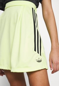 Ljusgrön sportkjol i ett mjukt material, med svarta sidostråkar och en broderad logotyp på fållen. Urringad design med veck.