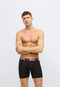 Czarne bokserki z czerwoną i białą gumą w pasie z logo "DIESEL", wykonane z gładkiej tkaniny, o dopasowanym kroju i długości do połowy uda.