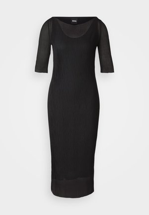 Abito nero con scollo a barca, maniche a tre quarti e texture a pieghe verticali. Lungo fino al ginocchio, con una silhouette aderente e dettagli trasparenti.