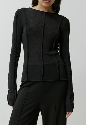 Schwarzes Langarmshirt aus geripptem Stoff, mit vertikalen Nähten, Rundhalsausschnitt und leicht ausladenden Manschetten. Dazu passende Hosen.