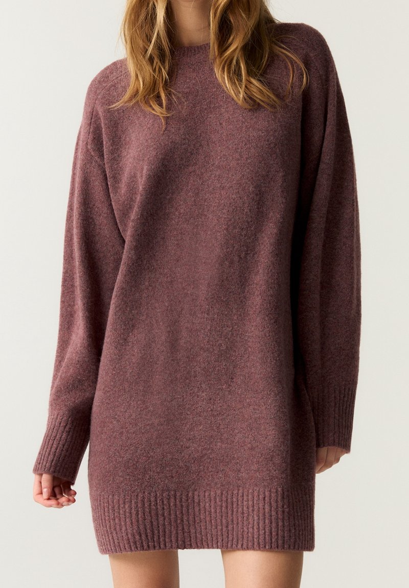 Robe pull de couleur rouille avec un col rond, des poignets et un ourlet côtelés. Coupe oversize avec une finition douce et texturée.