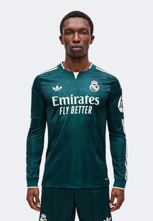 Uomo che indossa la maglia da calcio a maniche lunghe del Real Madrid verde scuro con logo bianco Emirates Fly Better e stemma del club sul petto.