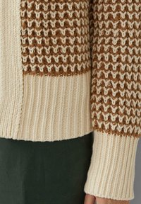Cremefarbener und brauner Strickpullover mit strukturiertem Muster. Gerippte Bündchen und Saum, kontrastierende Abschnitte und weiche, voluminöse Garnzusammensetzung.