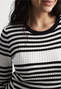 Gestreifter Strickpullover in Schwarz und Weiß mit geripptem Material und rundem Halsausschnitt, versehen mit abwechselnd breiten und schmalen Streifen.