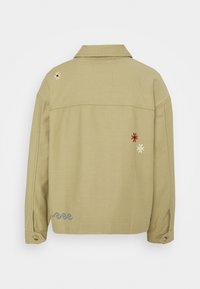 Beżowa kurtka z długim rękawem i kołnierzykiem, z małymi haftowanymi wzorami: żółty i biały kwiat, czerwony kwiat oraz niebieskie fale.