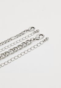 Zilveren metalen kettingen van verschillende diktes, met grote en kleine ovale schakels, voorzien van kreeftensluiting aan de uiteinden. Glad van textuur.