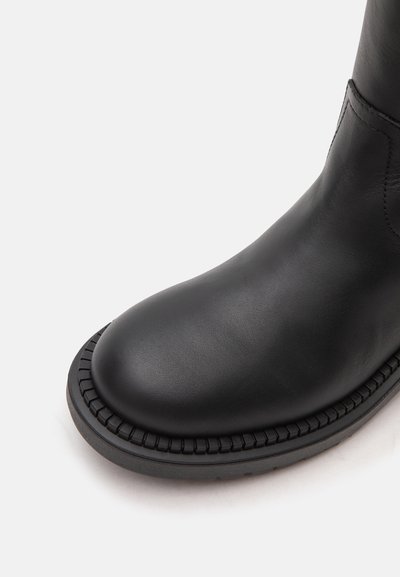 Gros plan sur la partie avant d'une botte en cuir noir avec un bout arrondi et un bord de semelle texturé.