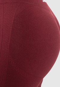 Zbliżenie winnych legginsów sportowych z teksturowanej tkaniny o dopasowanym kroju, podkreślające detale projektu i kolorystyki odzieży.