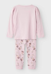 Ensemble de pyjama rose clair comprenant un haut à manches longues avec des manches bouffantes et un pantalon à motifs présentant des personnages de dessins animés, des lunes et des étoiles.