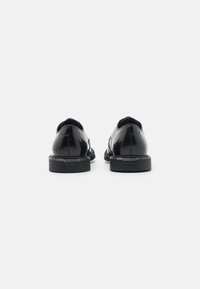 Chaussures en cuir verni noir avec une finition lisse et réfléchissante. Présentent un bout rond et une semelle en caoutchouc plate avec des détails de marque.