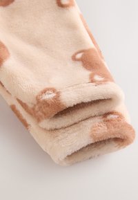 Tissu polaire beige doux avec des taches irrégulières marron clair, plié pour montrer la texture et l'épaisseur.