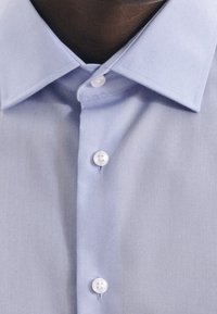 Lichtblauw overhemdd met een gladde textuur, een klassieke kraag en witte ronde knopen langs de sluiting.