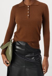Maglione marrone lavorato a maglia con collo a camicia, patta con cinque bottoni e maniche lunghe, abbinato a una gonna di pelle nera e una borsa verde.