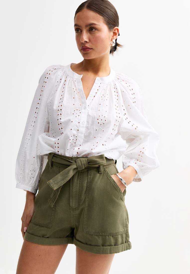 Vit bomullskjorta med hålmönster och samlade axlar, i kombination med olivgröna high-waisted shorts och ett knutet bälte.