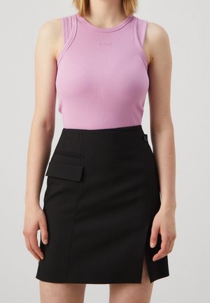 Mujer que lleva un top lila sin mangas con textura acanalada y una falda negra con abertura frontal y bolsillo con solapa.