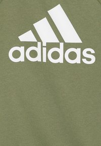 Sudadera verde oliva con un acabado texturizado que presenta un gran logo blanco de Adidas y tres rayas diagonales blancas en la parte superior izquierda.
