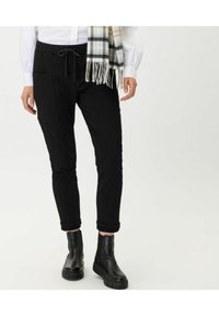 Pantalones de chándal negros con cintura elástica y cordón, que cuentan con bolsillos laterales, corte ajustado y puños enrollados. Combinados con botas negras hasta el tobillo.