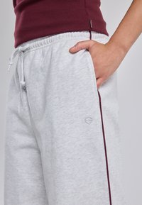 Light grey sweatpants with a textured finish, elastic waistband, adjustable drawstring, and a maroon side stripe. Small logo detail on pocket.