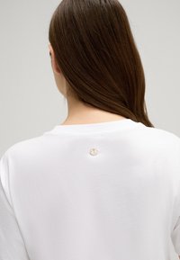 Witte katoenen t-shirt met een ronde halslijn, voorzien van een klein geborduurd logo op de achterkant. Zachte textuur en een ontspannen pasvorm.