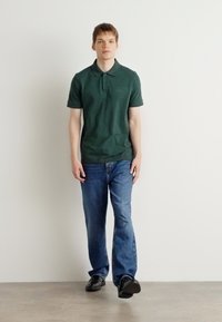 Grønn polo skjorte med krage, paret med blå jeans. Poloen har en subtil brodert logo, og jeansene har en klassisk passform.