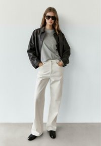 Svart läderjacka, grå t-shirt, vita jeans med vida ben, svarta skor och stora solglasögon; minimalistisk design, släta texturer, neutrala färger.