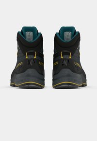 Melni un pelēki pārgājienu apavi ar augstu potīti, kas izceļas ar teksturētu virsmu, dzelteniem akcentiem un izturīgu gumijas zoli.