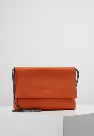 Oranje leren crossbodytas met klepsluiting en dun zwart-wit gevlochten bandje op een wit voetstuk tegen een grijze achtergrond.
