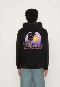 Svart hoodie med dragsko, med en färgglad grafik av en palm och sol på baksidan. Slät textur, avslappnad passform, ribbad fåll.