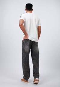 Hvit t-skjorte for menn, kort erme, kombinert med løst sittende, falmet grå jeans og brune joggesko. Enkelt design med minimal detaljering.