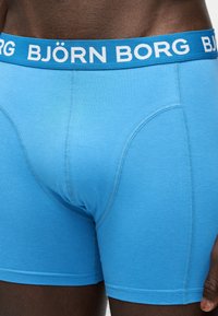 Gros plan sur une personne portant un boxer bleu vif avec une ceinture bleu comportant le texte blanc "BJÖRN BORG".