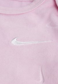 Rožnata flisna tkanina z srebrnim vezenim logotipom Nike swoosh. Material je mehak s prijetno teksturo in okroglo izrezom na vratu.