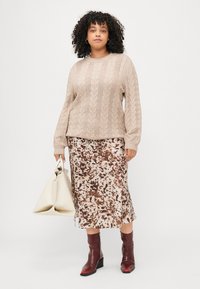 Beige svetr s pleteným vzorem, vzorovaná midi sukně v hnědé a krémové barvě, vínové kotníkové boty a krémová taška. Hladké textury a vrstvený design.
