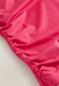 Tissu rose vif avec une texture lisse, présentant un détail froncé le long du bord. Matériau léger et flexible.