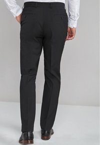 Pantalons tailleur noirs avec une texture lisse, dotés de deux poches arrière et d'une coupe droite. Portés avec des chaussures noires vernis.